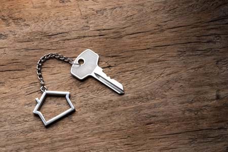 Key attached to a key ring shaped like a house on a timber surface.